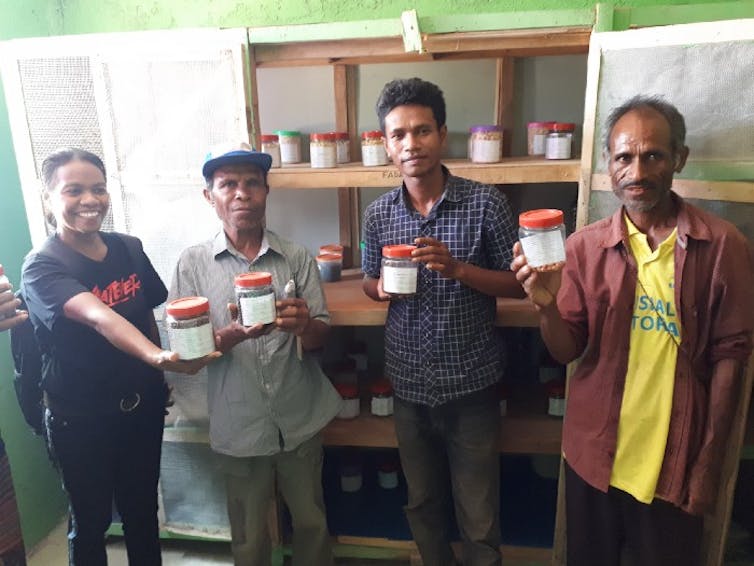 A woman and two men hold jars of seeds