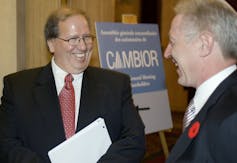 Two men in suits smile as they chat with a Cambior sign behind them.