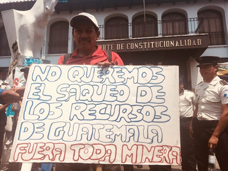 A man holds a sign in Spanish outside a courthouse that reads 'We do not want the looting of Guatemalan resources.'