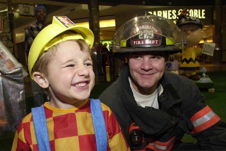 A boy dressed as a firefighter standing next to a real firefighter.