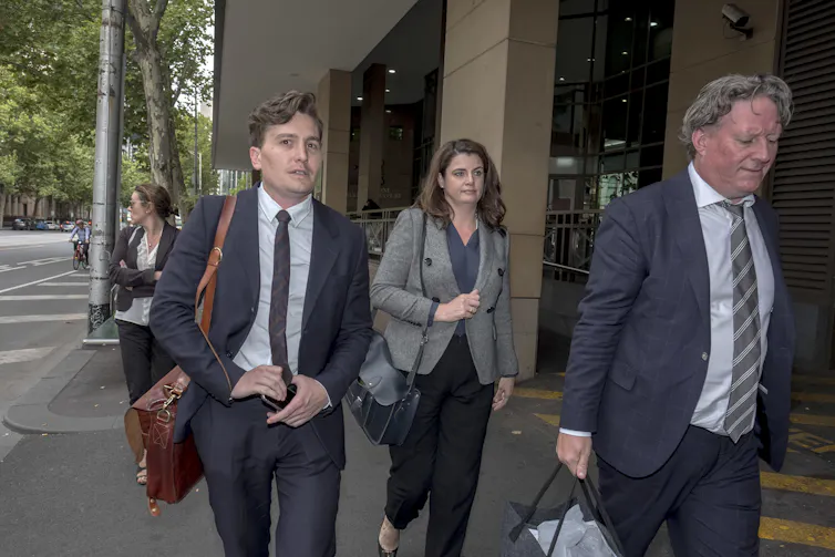 Milligan, centre, walking between two men in suits.