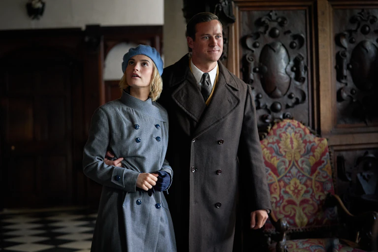 Woman and man in 1940s costumes stand in the entrance hall of a stately home.