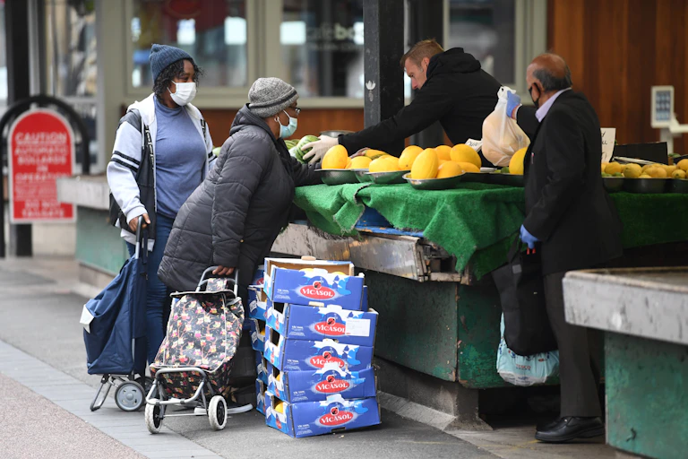 Two black women and an Asian man shop at a market stall.