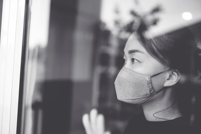 A woman wearing a mask looks out of a window.
