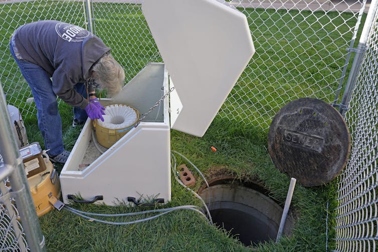 A man bending over a machine with tubes running into an open sewer.