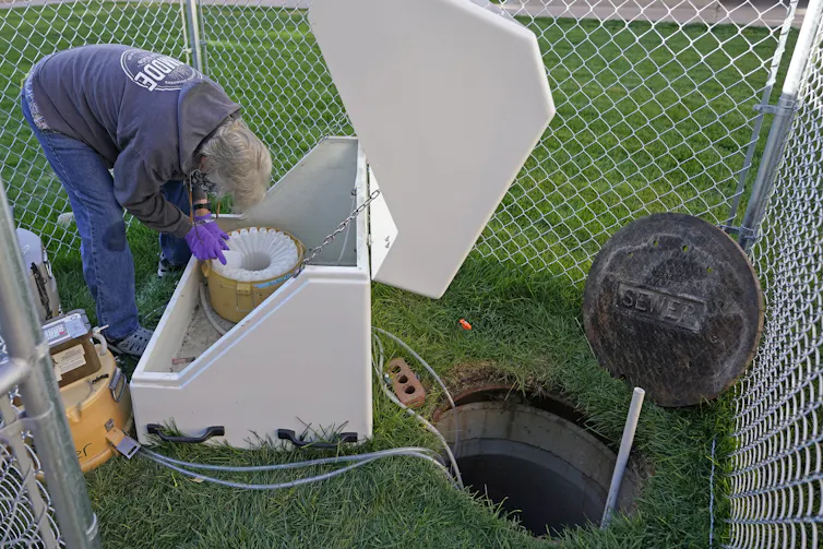 A man bending over a machine with tubes running into an open sewer.