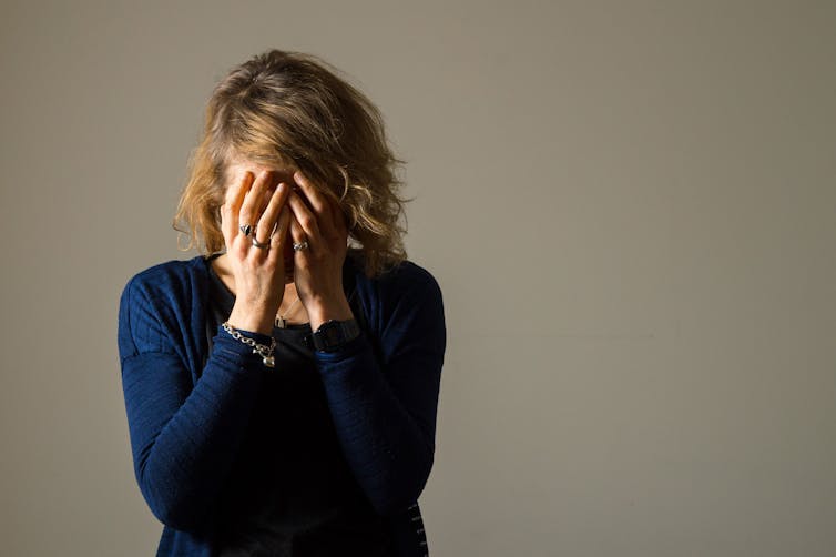 A woman wearing a blue sweater with her head in her hands.