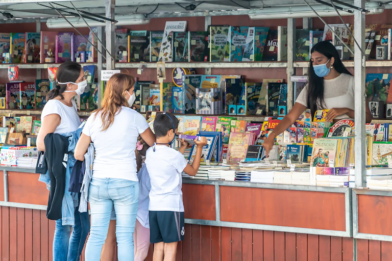 Tres personas con mascarilla ante un puesto de la feria del libro de Punta Umbría (Huelva)
