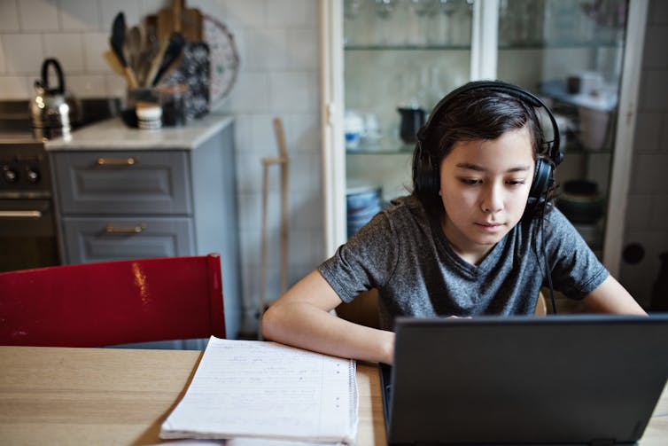 A boy works on a laptop at a table in his home.]