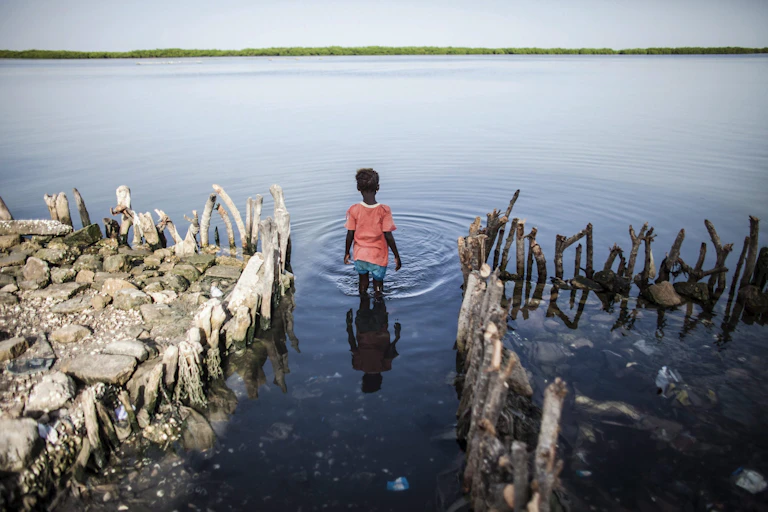 A girl wading in the water in front of an inundated home.