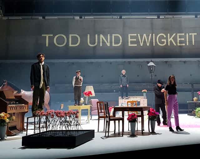 Production image, cast on stage looks to audience