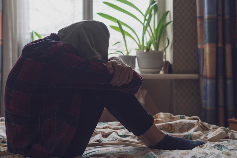 Sad person sat on bed with head on knees