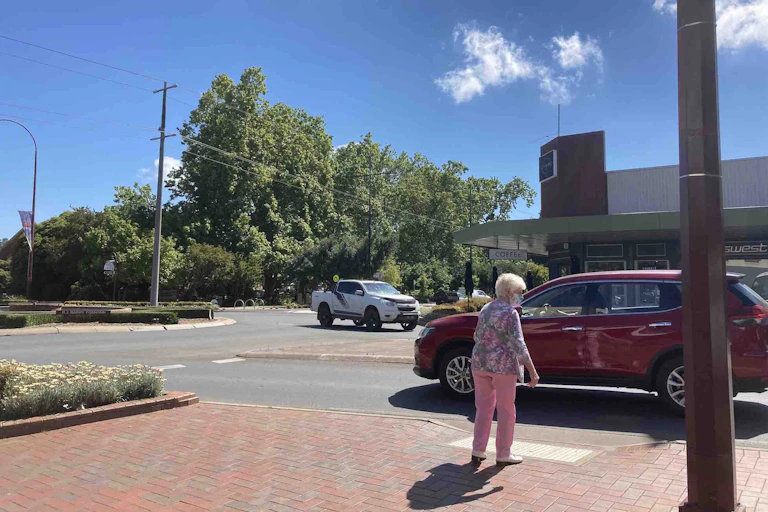 Older woman waits for traffic as she tries to cross the road