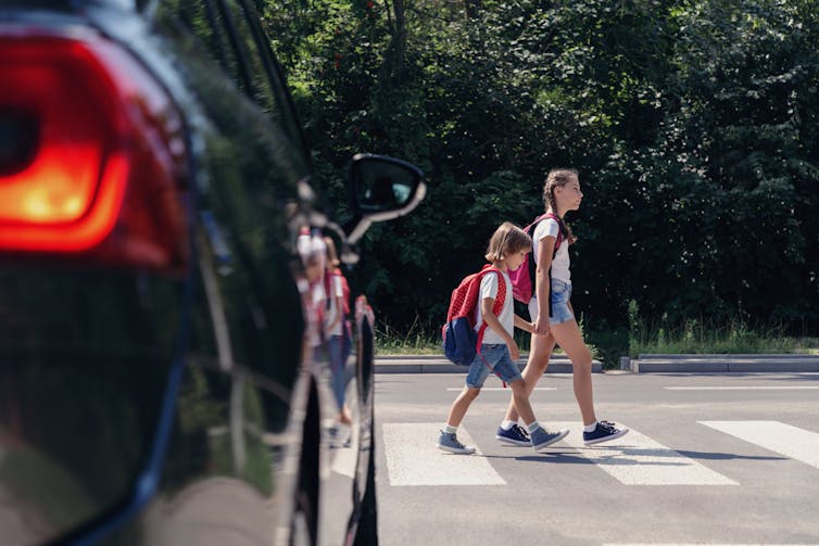 Children cross the road in front of a car.