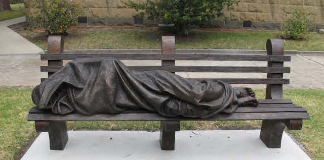 a bronze sculpture is shown prone on a park bench.