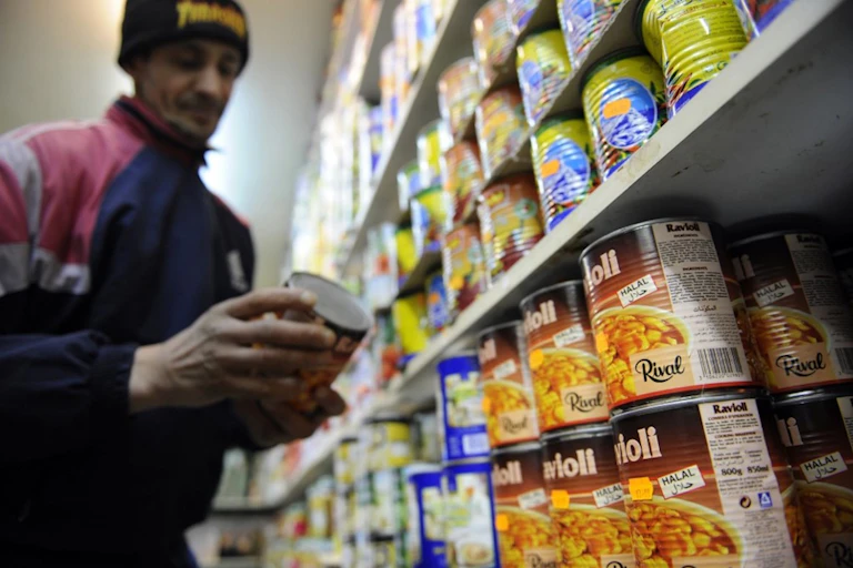 Un commerçant range une boite de conserve de nourriture halal dans un rayon