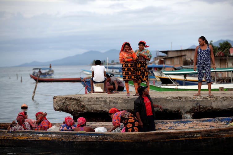 A group of women in colourful clothing board a canoe.