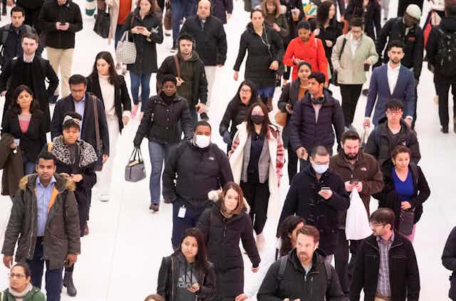 A crowd of people walking with only a few wearing masks.