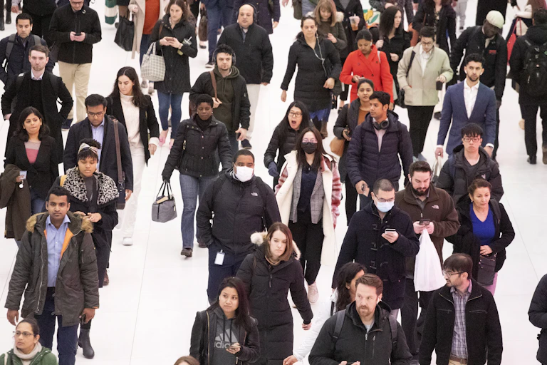A crowd of people walking with only a few wearing masks.