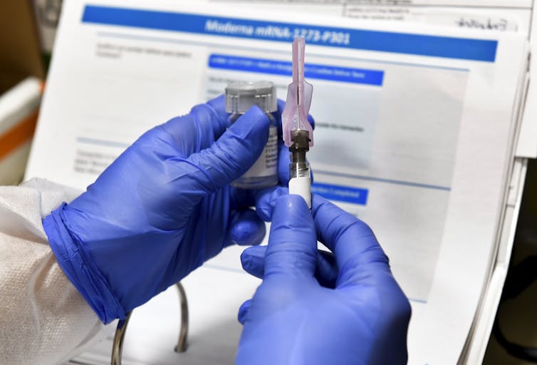 Two gloved hands holding a syringe and vaccine vial.