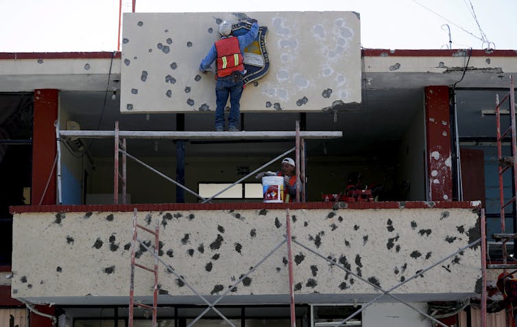 Workers repair the facade of a government building riddled with bullet holes.