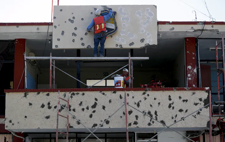 Workers repair the facade of a government building riddled with bullet holes.