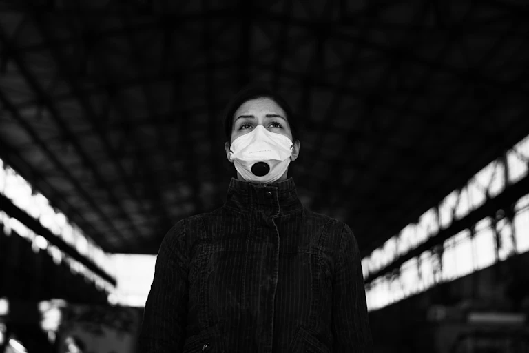 Foto en blanco y negro de una mujer con mascarilla dentro de una nave mirando al infinito.