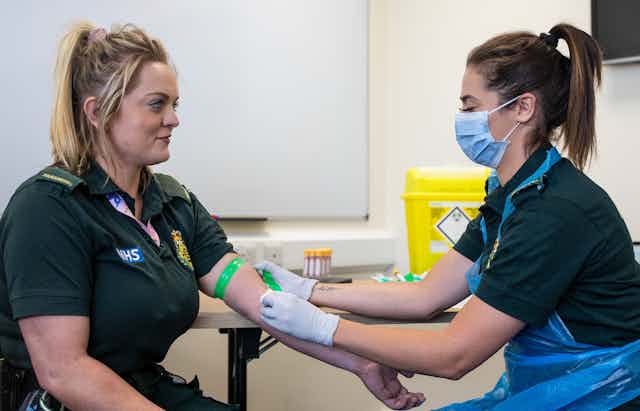 A paramedic taking a blood sample from another paramedic for an antibody test