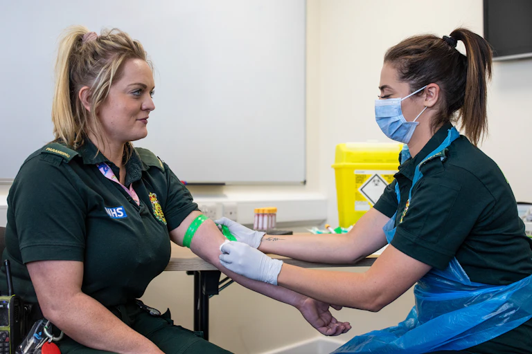 A paramedic taking a blood sample from another paramedic for an antibody test