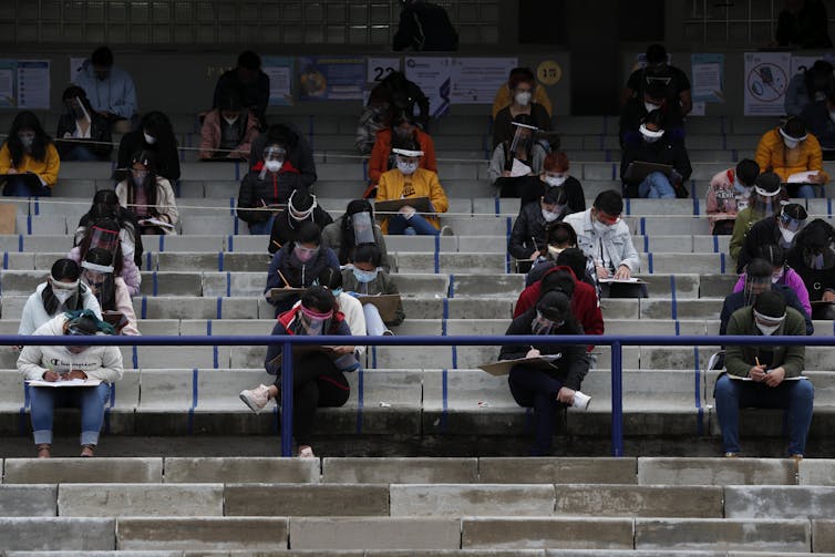 Students sit in an outdoor stadium writing entrance exams.