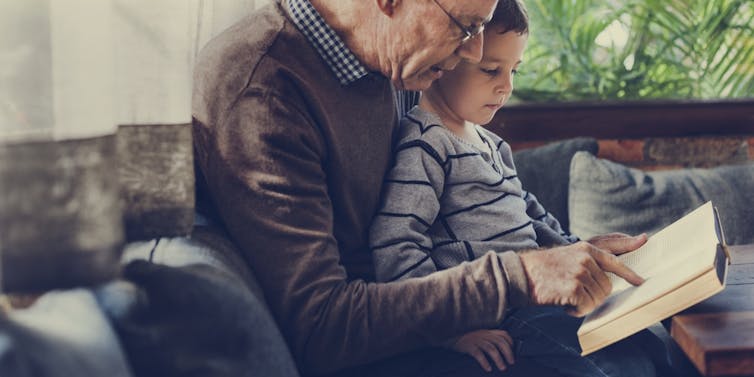 Child sitting on grandfather's lap reading together
