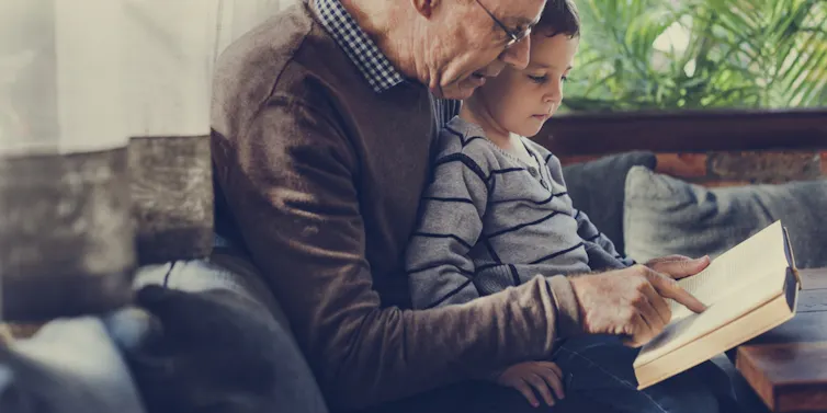 Child sitting on grandfather's lap reading together