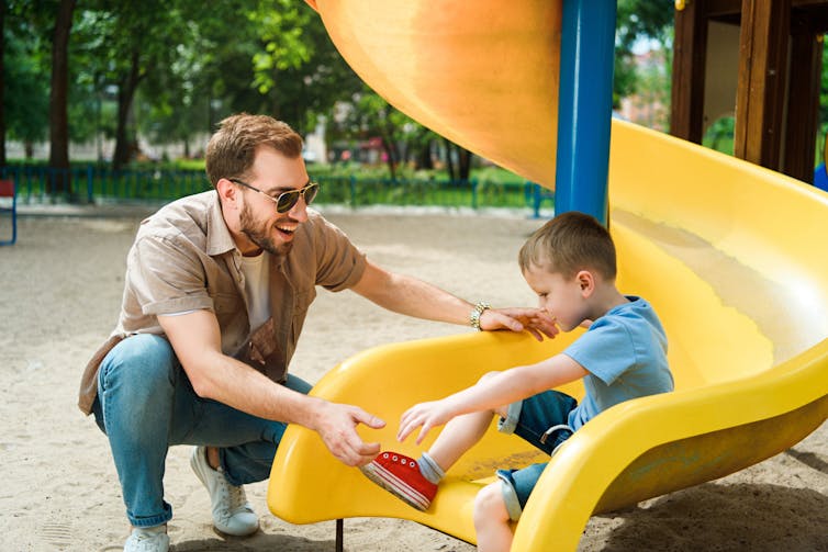 A man meets his son at the end of a slide.