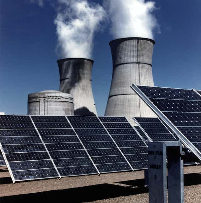 Nuclear power plant cooling towers loom over solar panels.