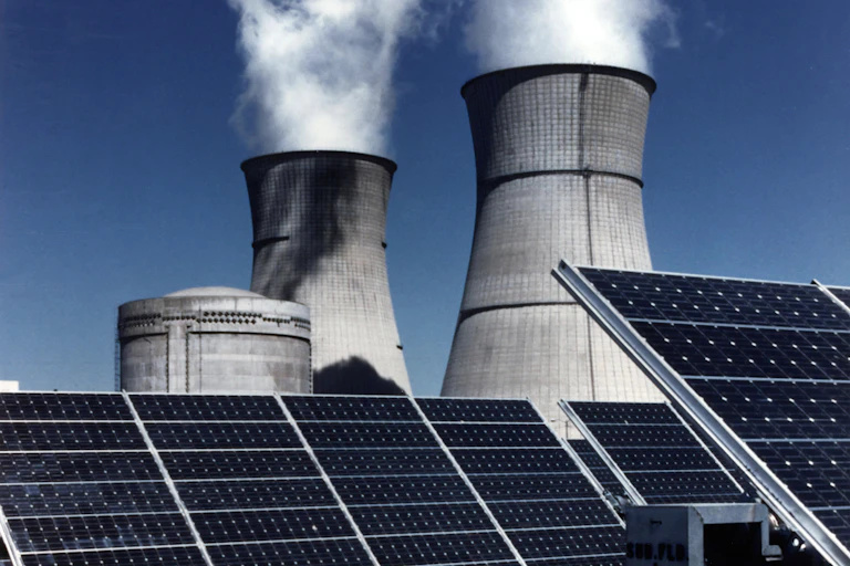 Nuclear power plant cooling towers loom over solar panels.