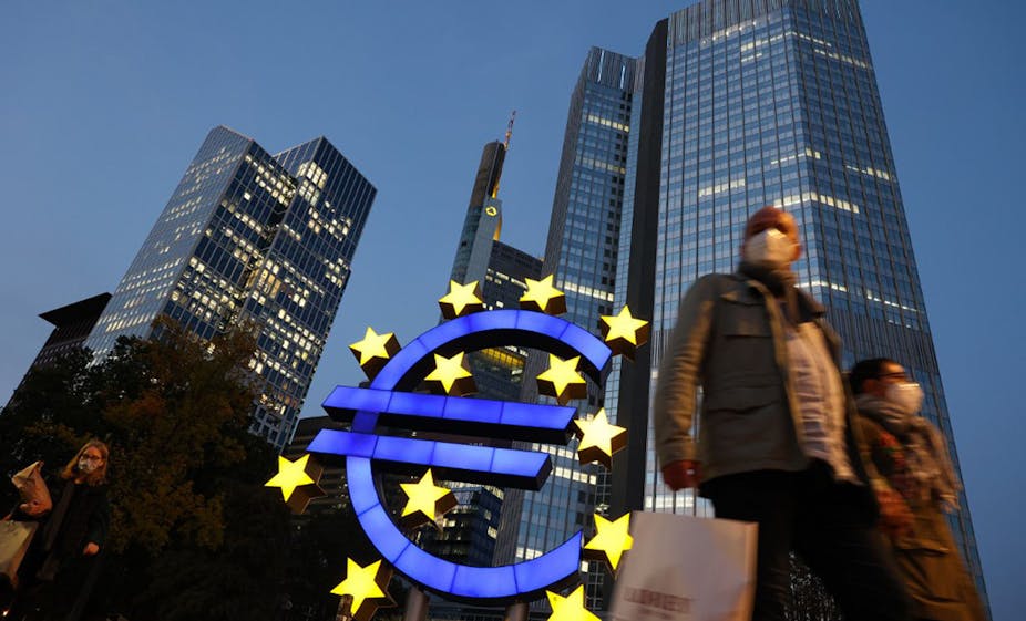 People wearing face masks walk in front of a euro sign in the center of Frankfurt am Main, Germany