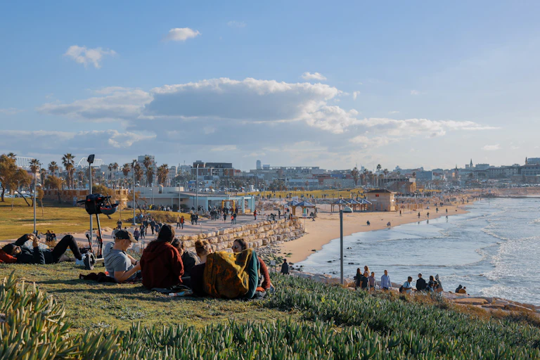 Young people sitting on grass bank overlooking a beach.