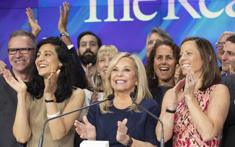 Ten smiling people in business attire pose together and clap their hands.