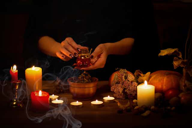 A manicured hand holding a potion amid smoke and candles