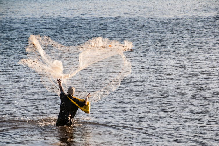 A man using a cast net to fish in the sea.