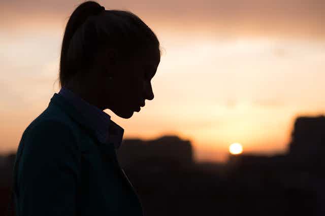 A young woman's silhouette with a blurry urban sunset in the background.