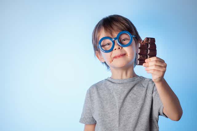 Young boy wearing glasses eating chocolate.