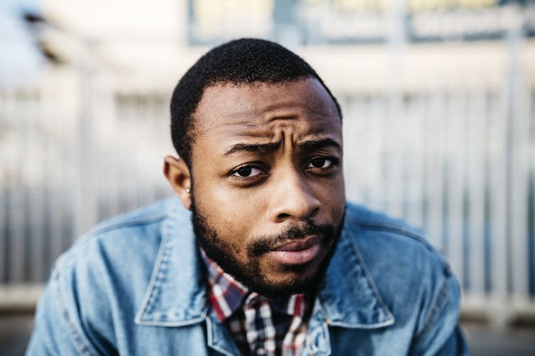 A man in a beard wearing a jean jacket looking quizzical.