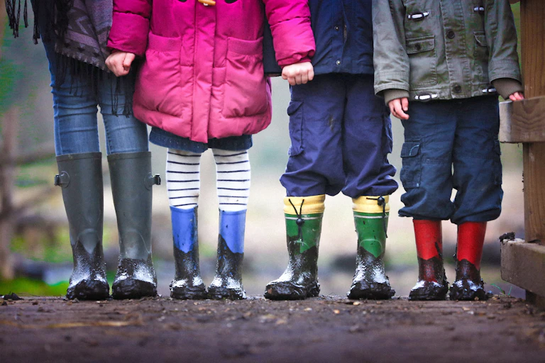 Children in rainboots are seen from the neck down standing in a row.
