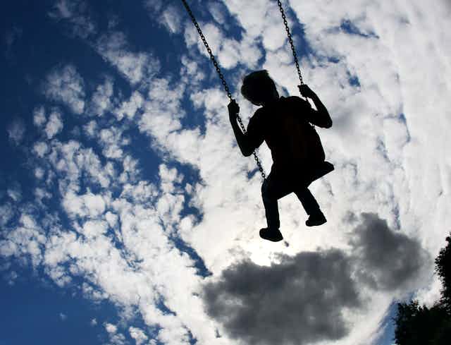 A child seen on swings under a blue sky with clouds on a playground.