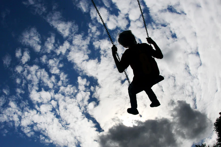 A child seen on swings under a blue sky with clouds on a playground.