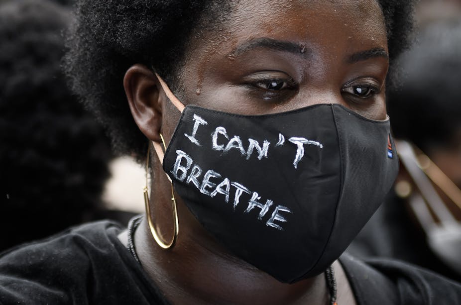 Close up of an exhausted looking black woman wearing a mask with "I CAN'T BREATHE" written on it.