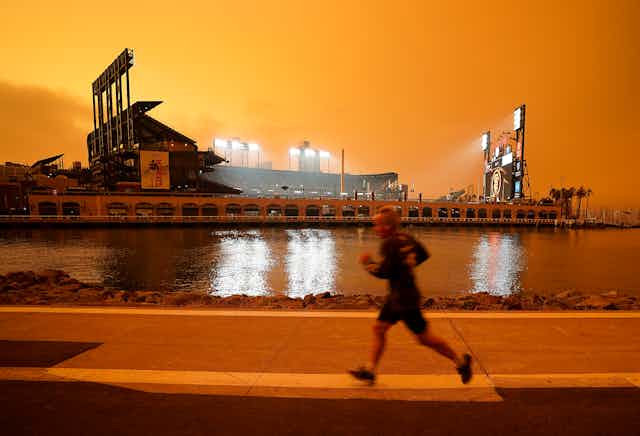 A person is seen running along the McCovey Cove in San Francisco under a burnt orange sky darkened by wildfire smoke.  
