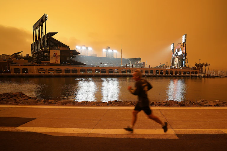 A person is seen running along the McCovey Cove in San Francisco under a burnt orange sky darkened by wildfire smoke.