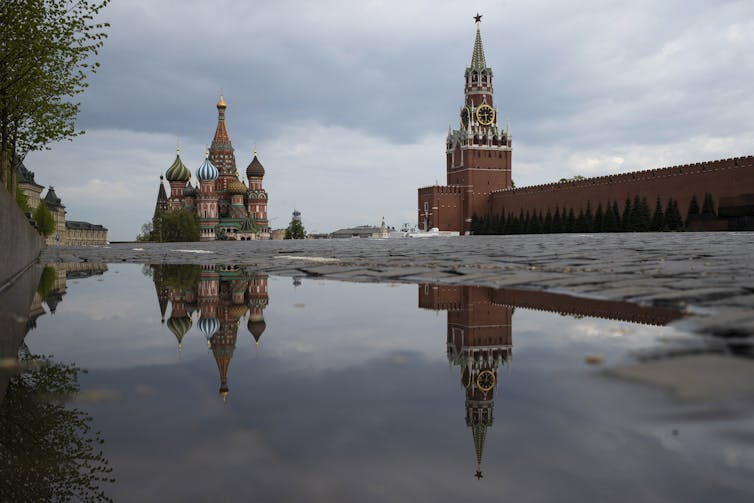 the Kremlin's Spasskaya Tower and St. Basil's Cathedral reflected in rain water puddles in Red Square in Moscow, Russia